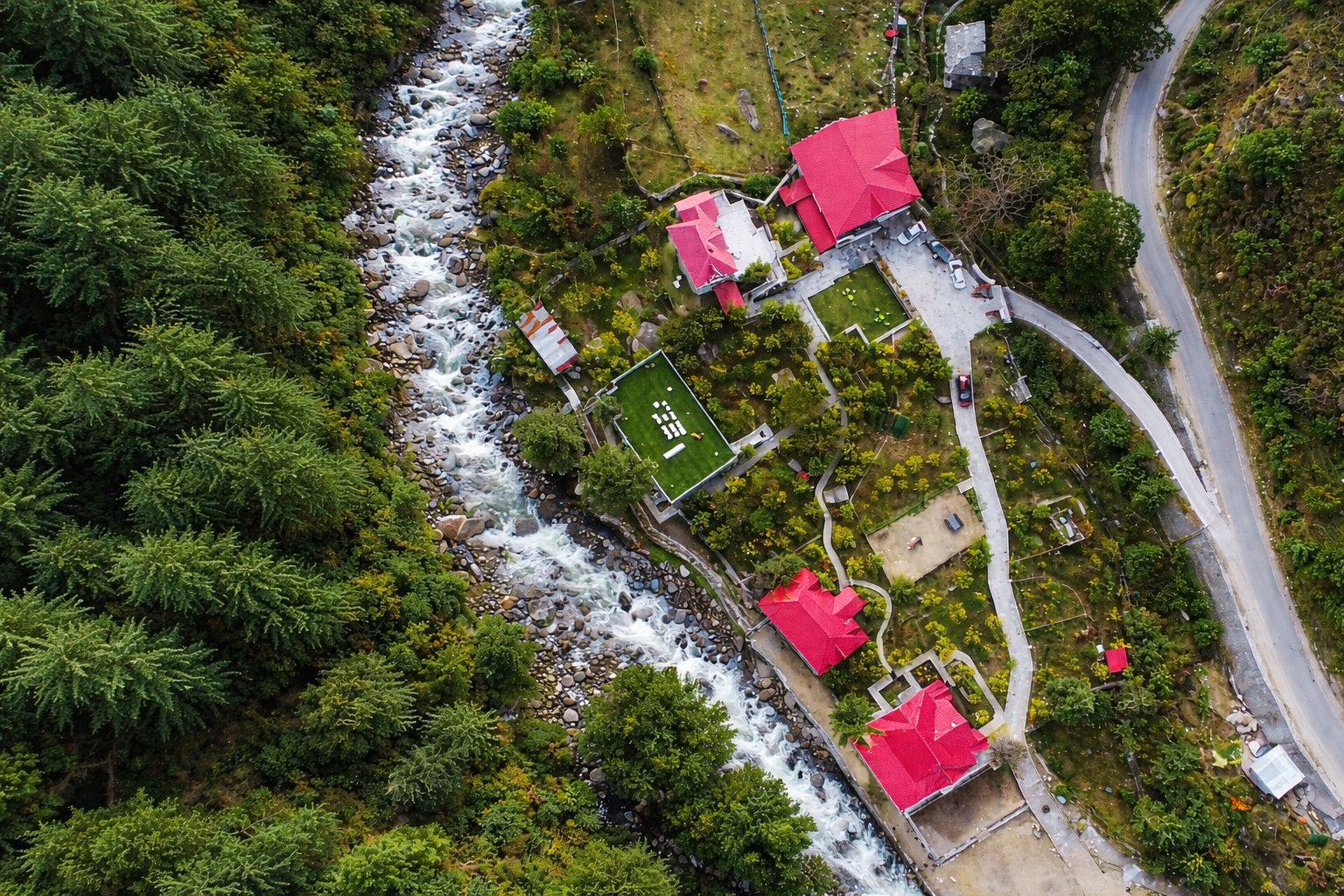 Aerial view of Anandgram Village’s red-roofed villas beside a mountain river in Pah Valley