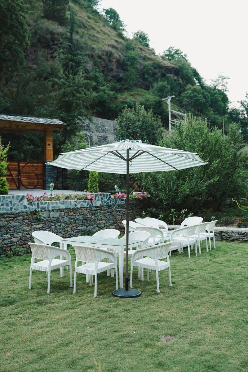 White lawn chairs under a striped umbrella
